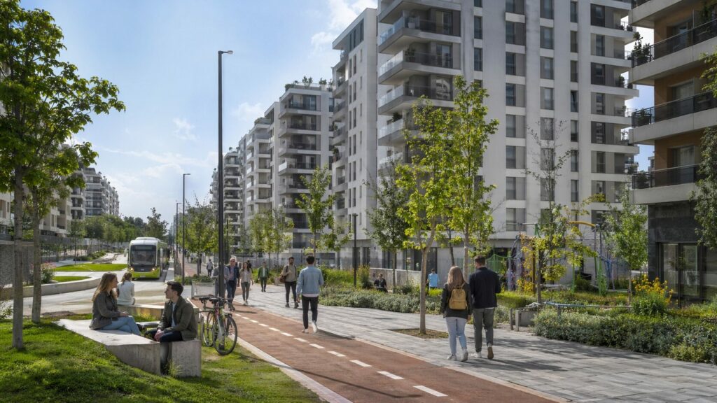 Imagen editorial de un entorno urbano contemporáneo en España, con varios edificios residenciales, presencia de jóvenes, en un entorne sostenible con una estética moderna vinculada al debate sobre vivienda asequible.